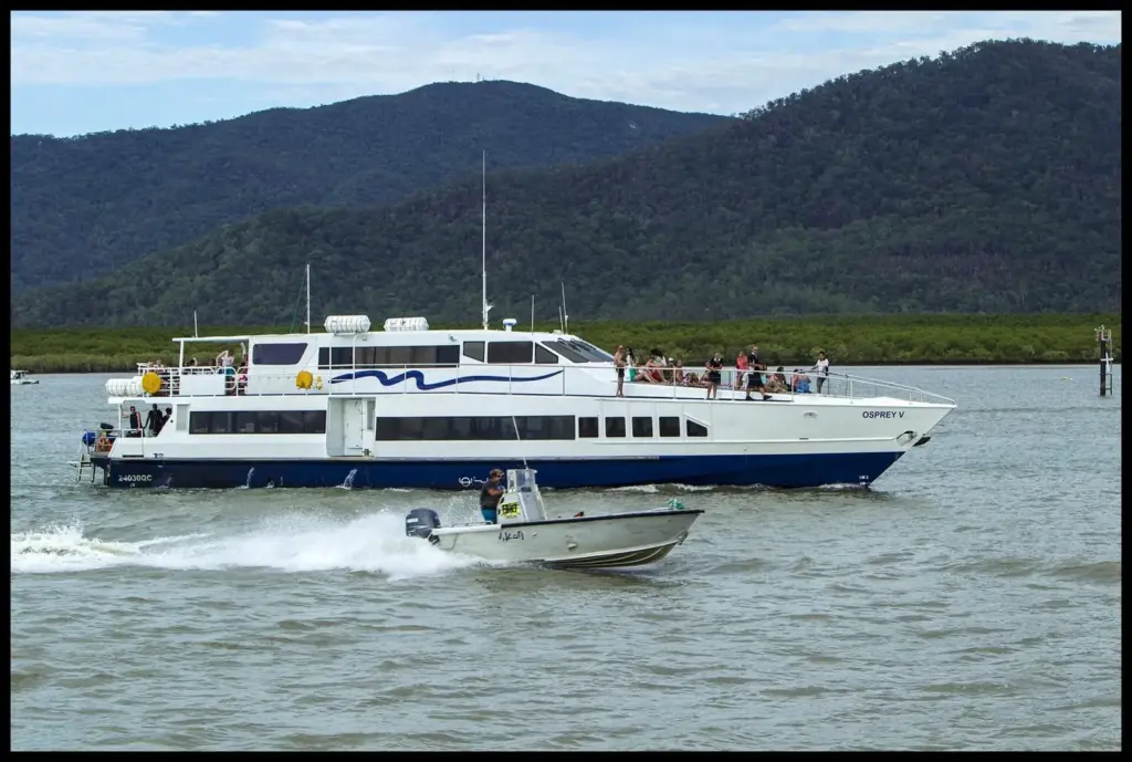 White reef catamaran and a small motorboat on the water at Cairns with green hills behind