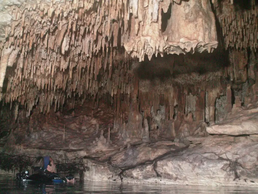 Stalactites crowding the ceiling of the Dome chamber at Cenote Chac Mool, with a diver at the water's surface below