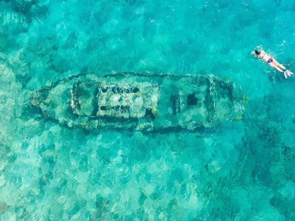Aerial view of the small Tugboat wreck in shallow turquoise water off Curaçao with a snorkeler nearby