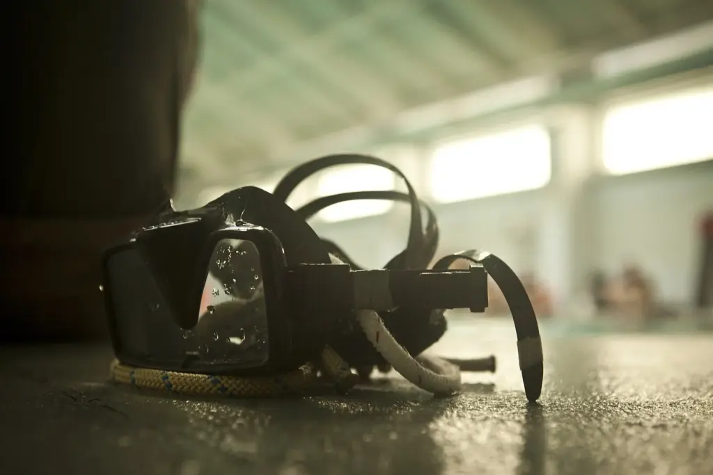 Dive mask with its strap coiled, resting on a wet pool deck before a confined water training session
