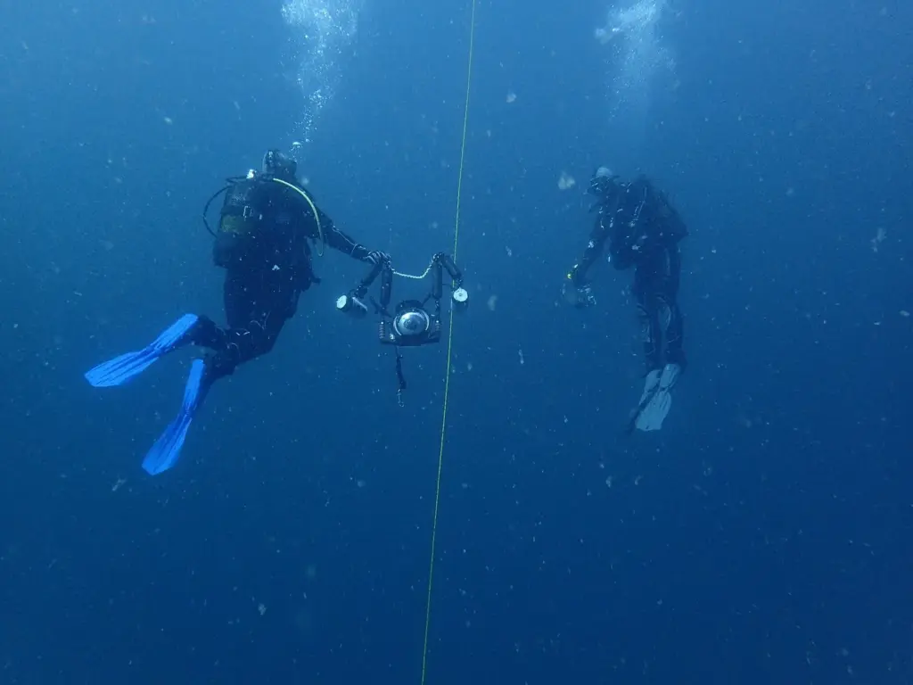 Two divers hovering beside a vertical line during a safety stop in blue open water