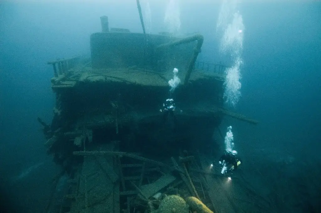 Divers with lights exploring the wooden superstructure of a shipwreck in Lake Huron's Thunder Bay National Marine Sanctuary