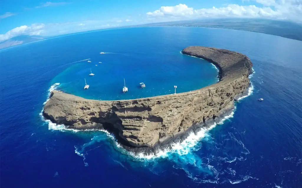 Aerial view of Molokini, a crescent-shaped volcanic crater off Maui, with dive and snorkel boats moored inside the cove