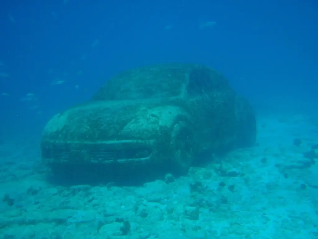 Algae-covered sculpture of a Volkswagen Beetle on the sandy seabed at the MUSA underwater museum near Cancun