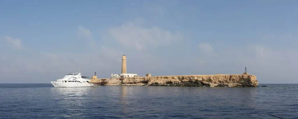 Big Brother island with its stone lighthouse and a dive liveaboard moored alongside in the Red Sea