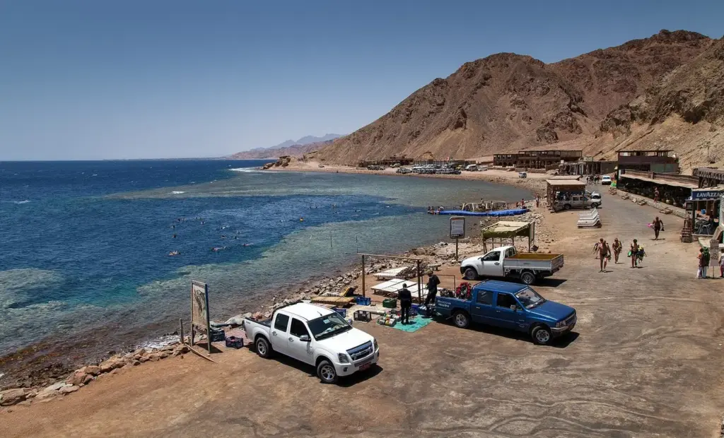 The shore at Dahab's Blue Hole with dive trucks, cafes and the deep blue water of the sinkhole beside the reef