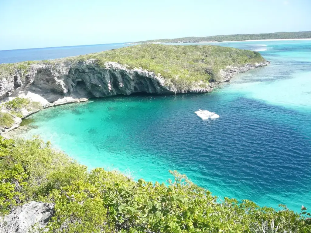 Deep blue circle of Dean's Blue Hole beside turquoise shallows and a limestone cliff on Long Island, Bahamas