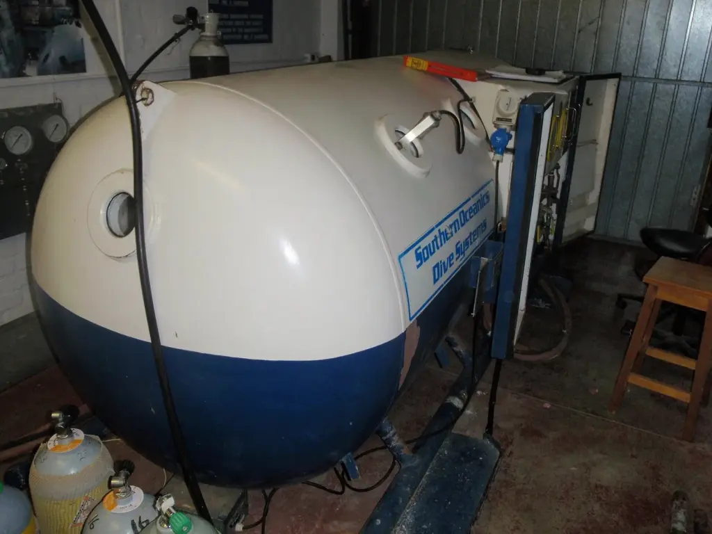 Small white and blue two-person deck decompression chamber inside a dive facility