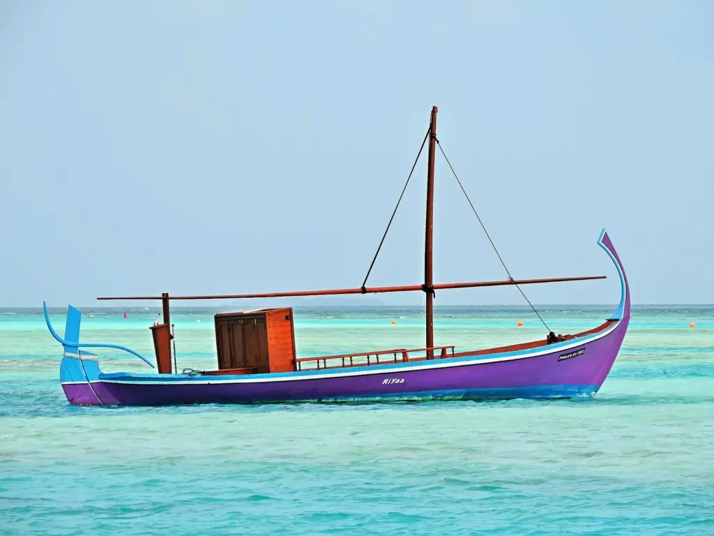 Traditional Maldivian dhoni boat with a tall mast moored on turquoise water