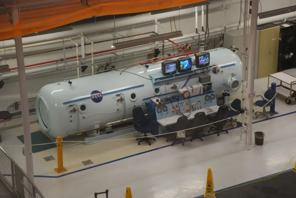 Large multiplace hyperbaric chamber with control panel and monitors in a treatment facility